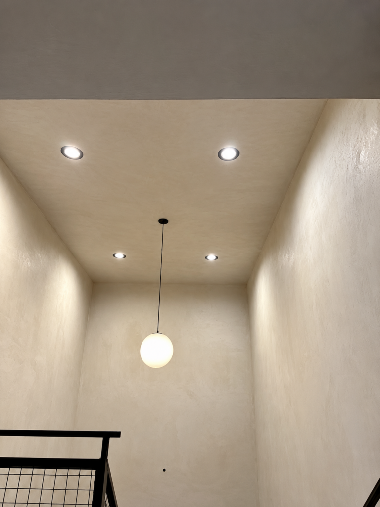 Finished plaster walls and recessed lighting around a stairwell